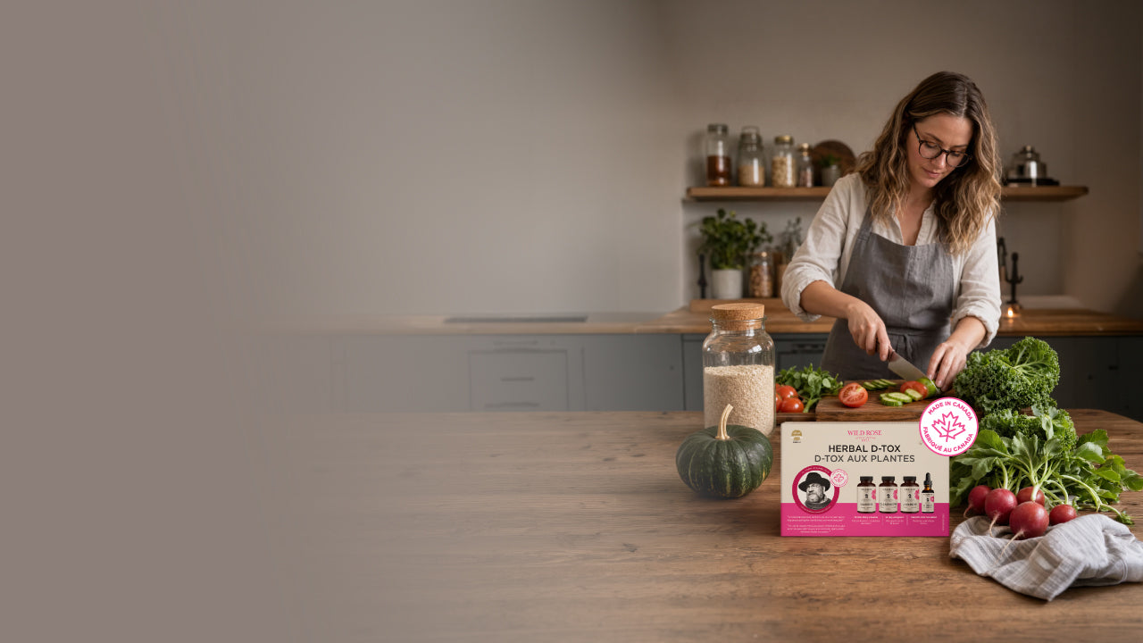 A woman in a kitchen wearing an apron while preparing fresh vegetables on a wooden table. In the foreground, a pink box labeled 'Herbal Dose' with four small bottles is placed next to a jar and a bag of radishes.